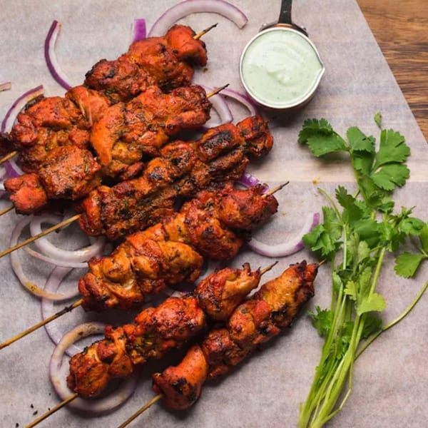 Indian chicken tikka skewers with red onion, cilantro, and a side of green chutney.