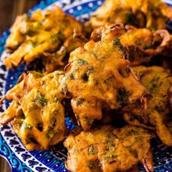 Close-up of golden-brown Indian pakoras with green herbs, served on a blue and white patterned plate.