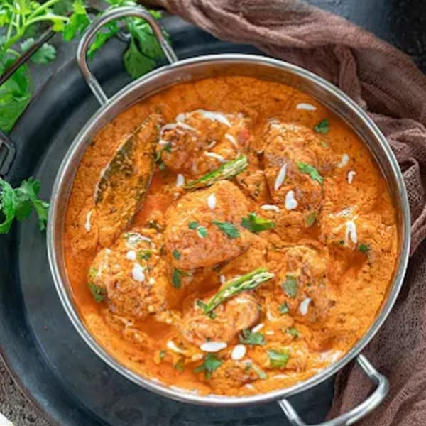 Desi Swaad Indian Restaurant's chicken curry, garnished with cream, green chilies, and cilantro.