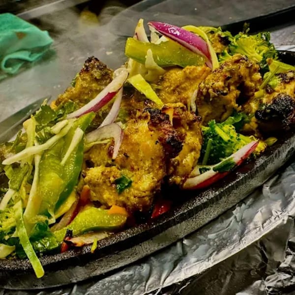 Sizzling Indian chicken tikka with onions, bell peppers, and broccoli on a hot platter.