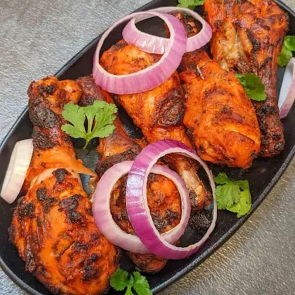 Desi Swaad's Indian Tandoori chicken drumsticks, garnished with red onion rings and cilantro.