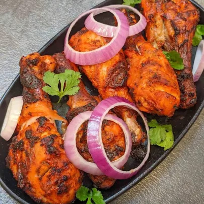 Desi Swaad's Indian Tandoori chicken drumsticks, garnished with red onion rings and cilantro.